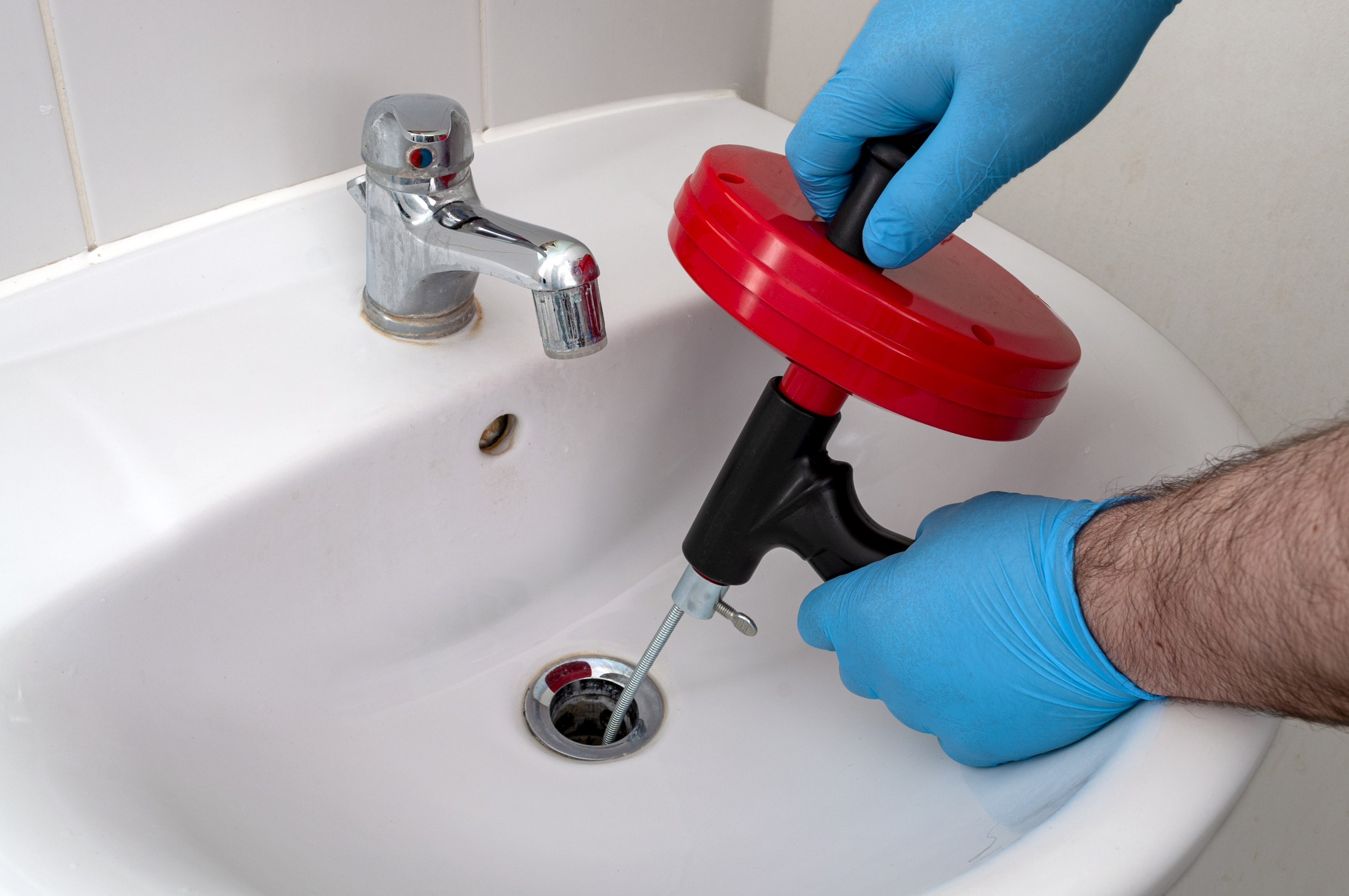 Blue-gloved plumber snaking a bathroom sink drain