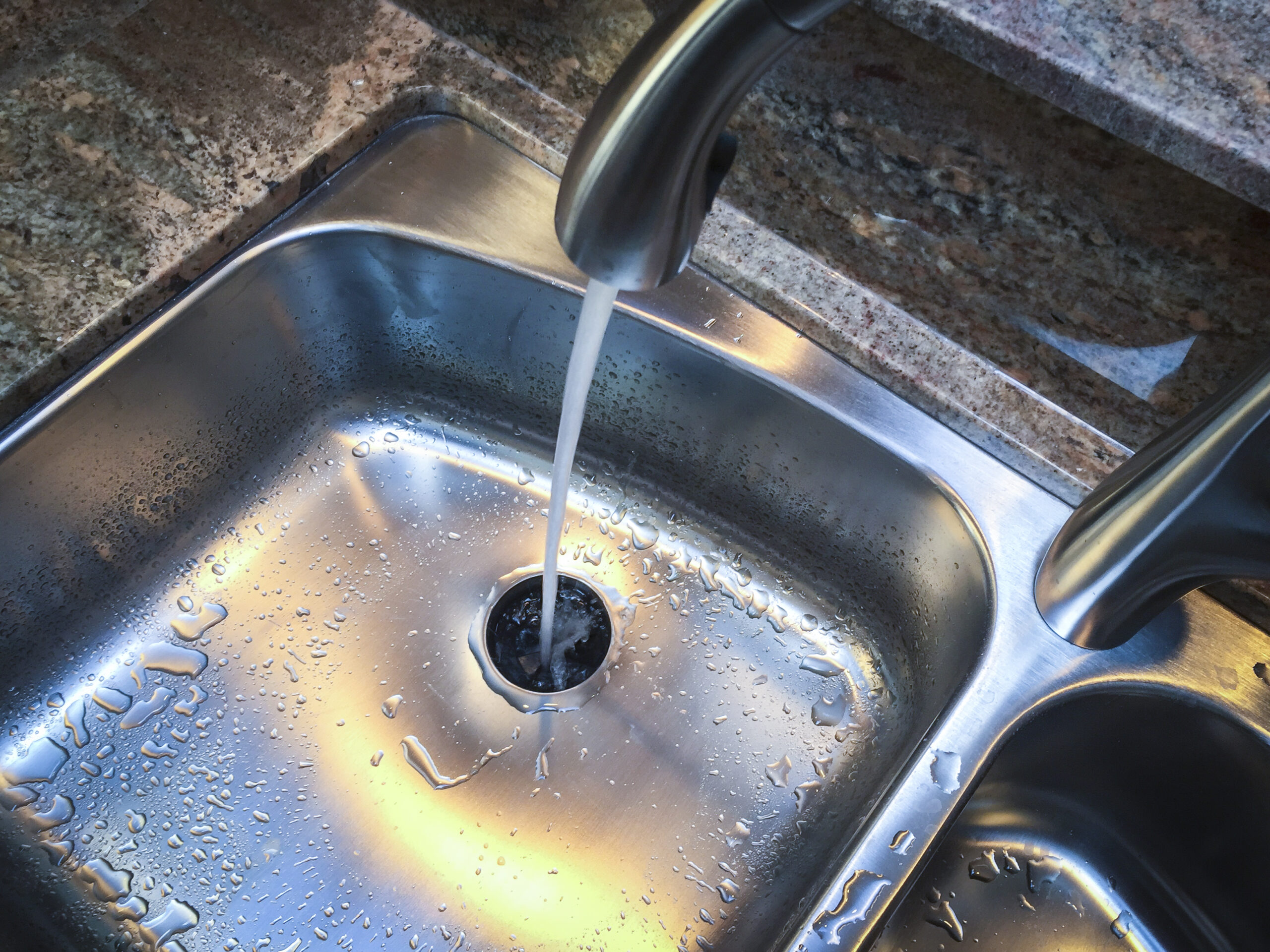 Stainless steel kitchen sink with garbage disposal and water running